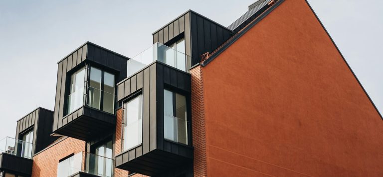 Edificio moderno con paredes rojas y balcones oscuros en la parte superior.